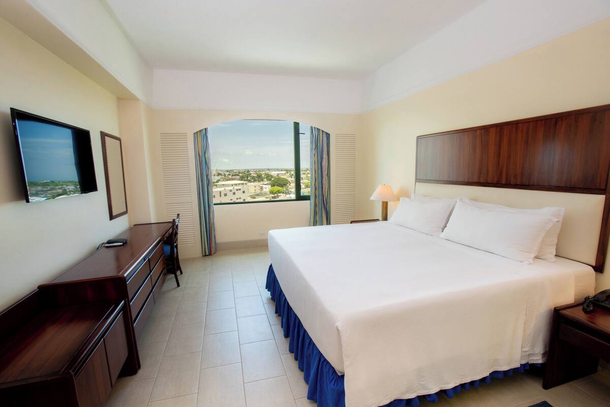 A hotel room with a large bed, a desk, a TV, and a window with curtains.