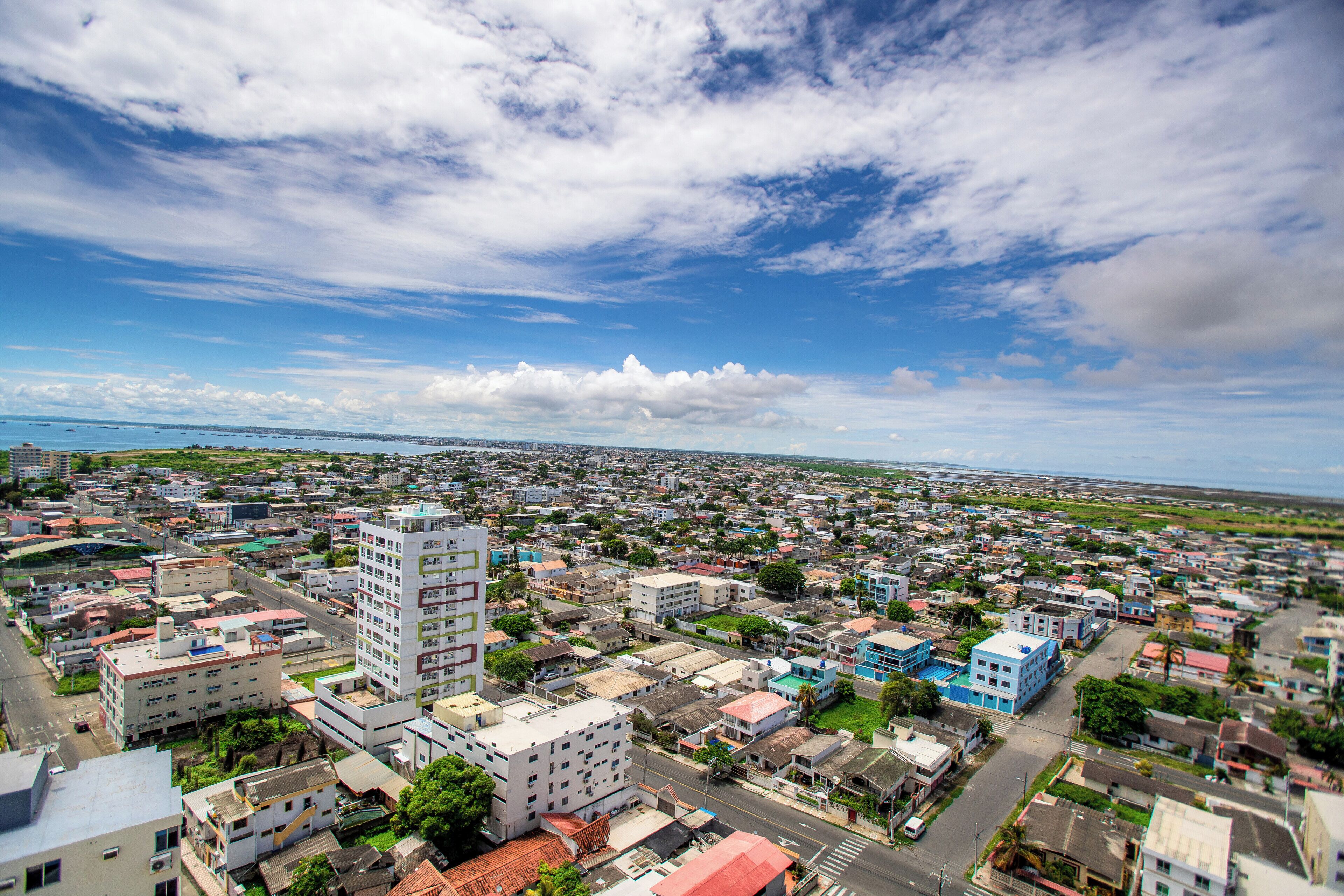 Un horizonte urbano con edificios residenciales y comerciales, cielo despejado y una vista distante del océano.