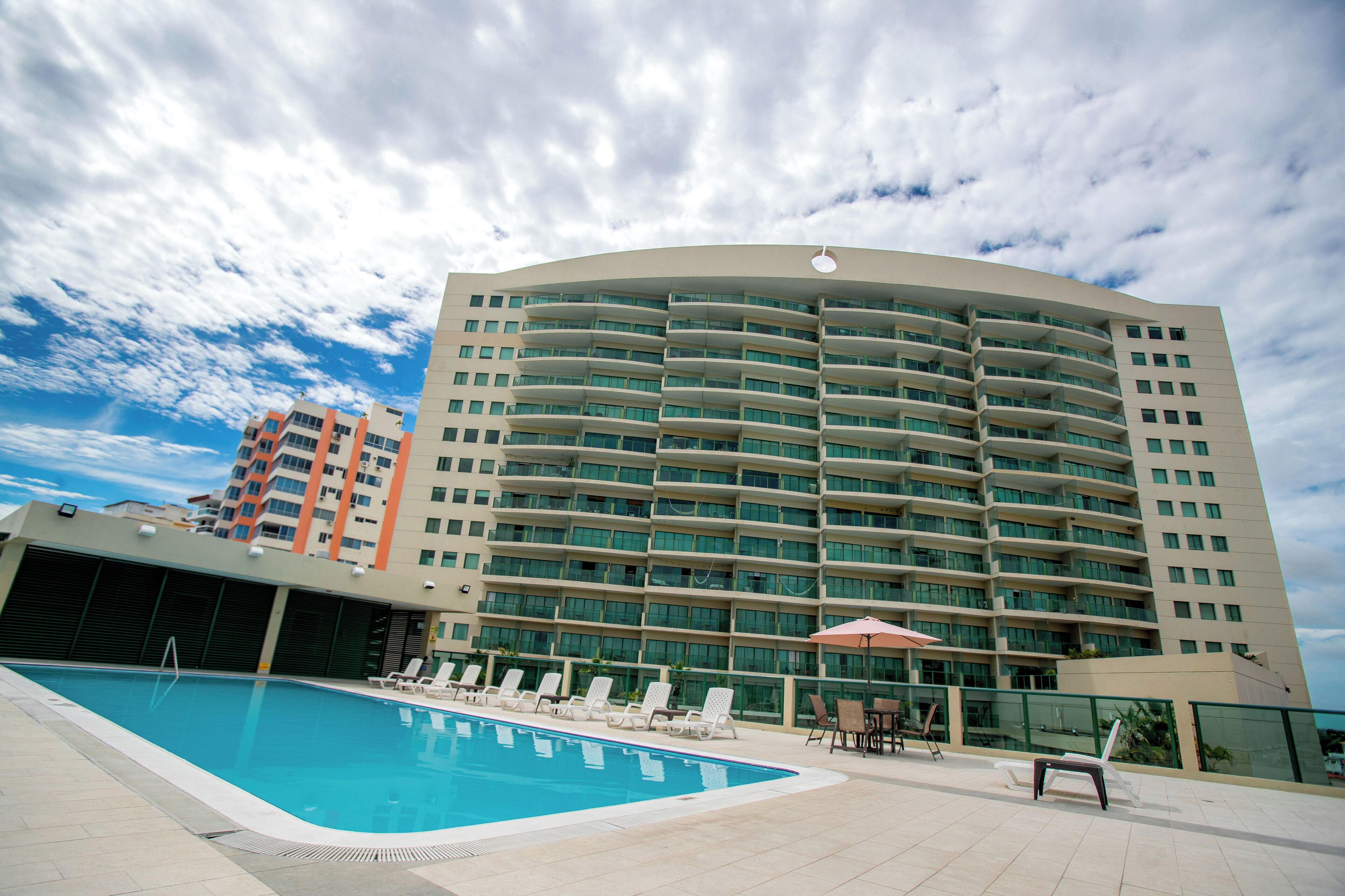 Un hotel moderno con piscina, sillas de descanso y fachada curva.
