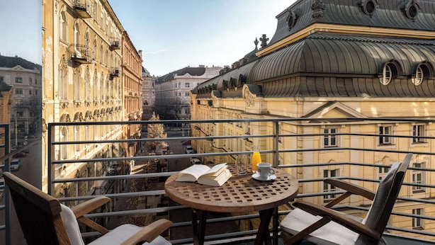 A balcony with a round table, two chairs, an open book, and a glass of orange juice. - NH Budapest City (Budapest)