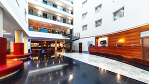 A spacious lobby with a modern design, featuring a reception desk, seating areas, and a staircase connecting multiple floors. - NH Budapest City (Budapest)