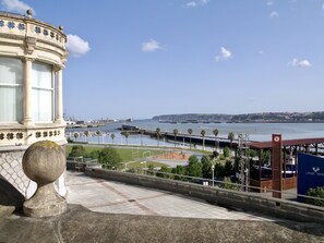 Vista costera con un edificio histórico, un puerto deportivo y cielo despejado.