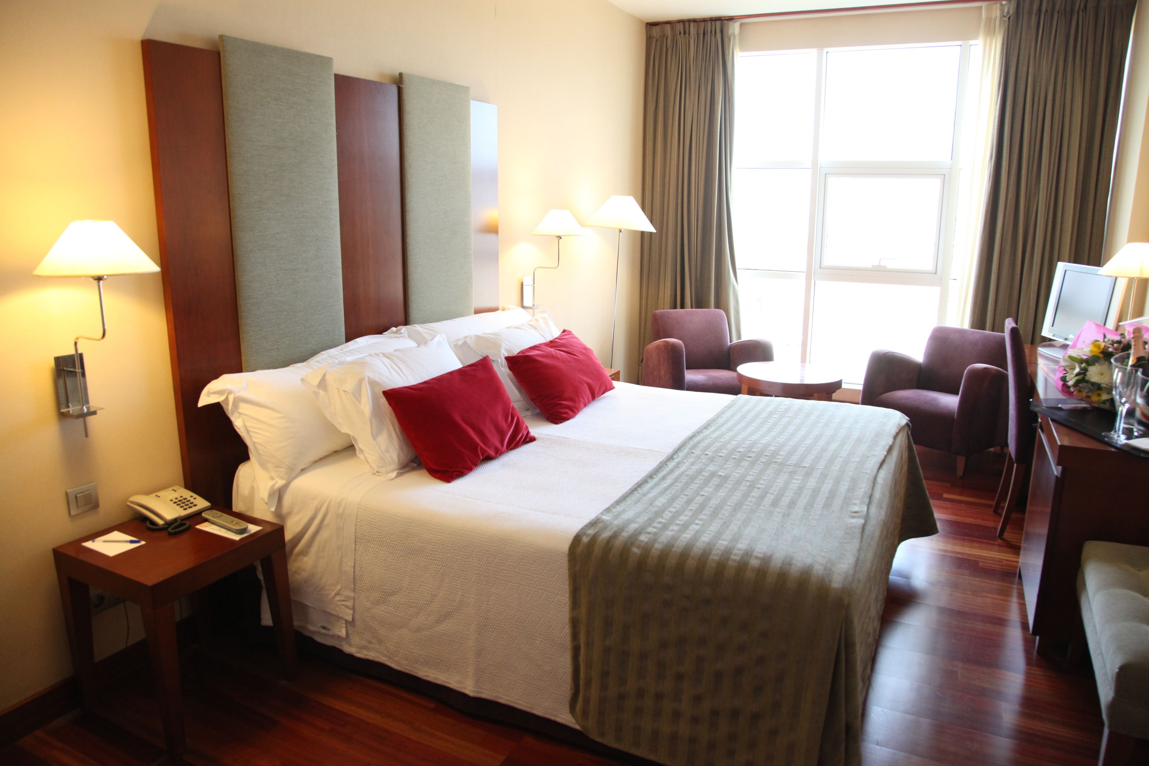 A hotel room with a large bed, two bedside tables, a desk with a chair, and a window with curtains.