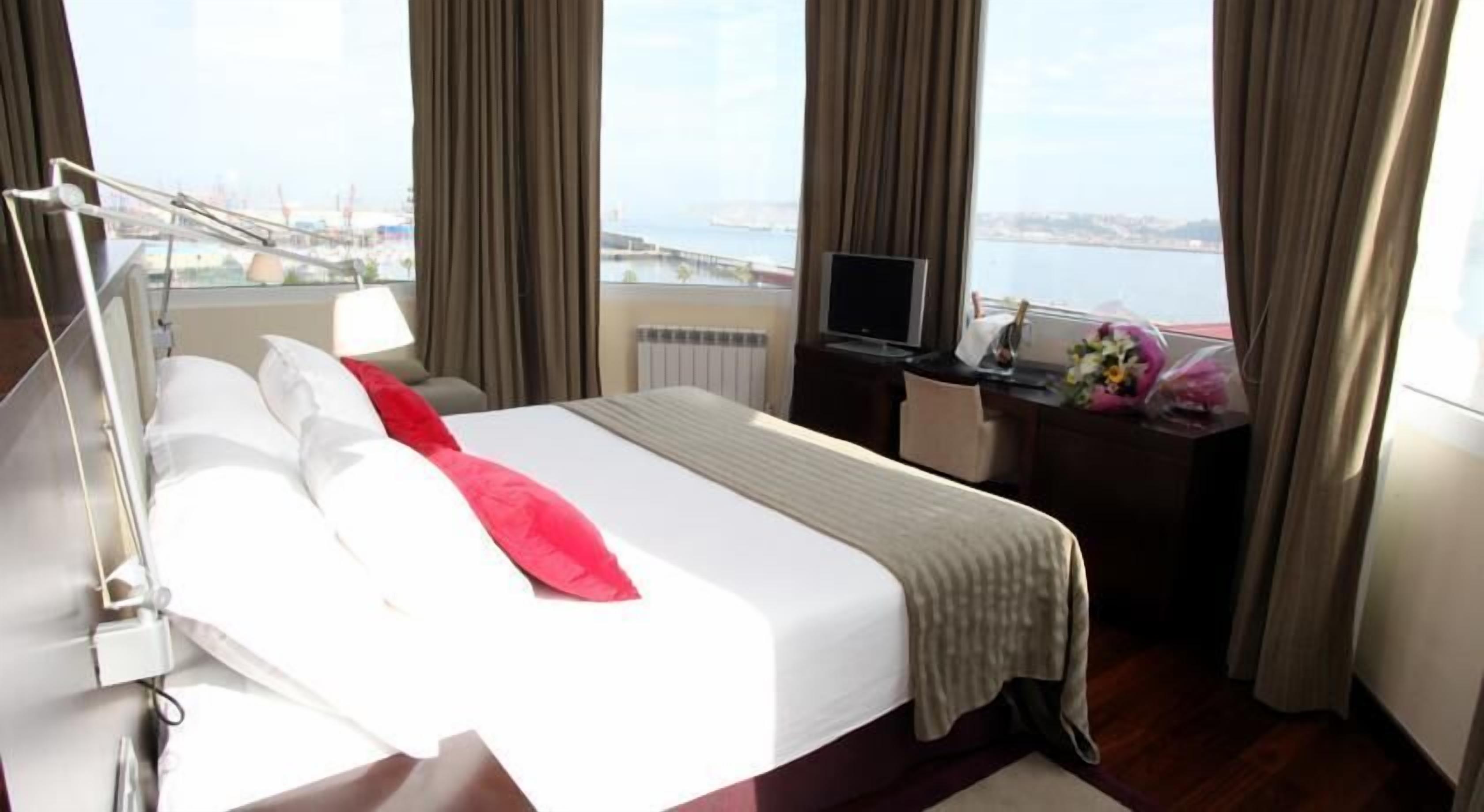 A hotel room with a bed, a desk with a computer, and a view of a body of water and a bridge.