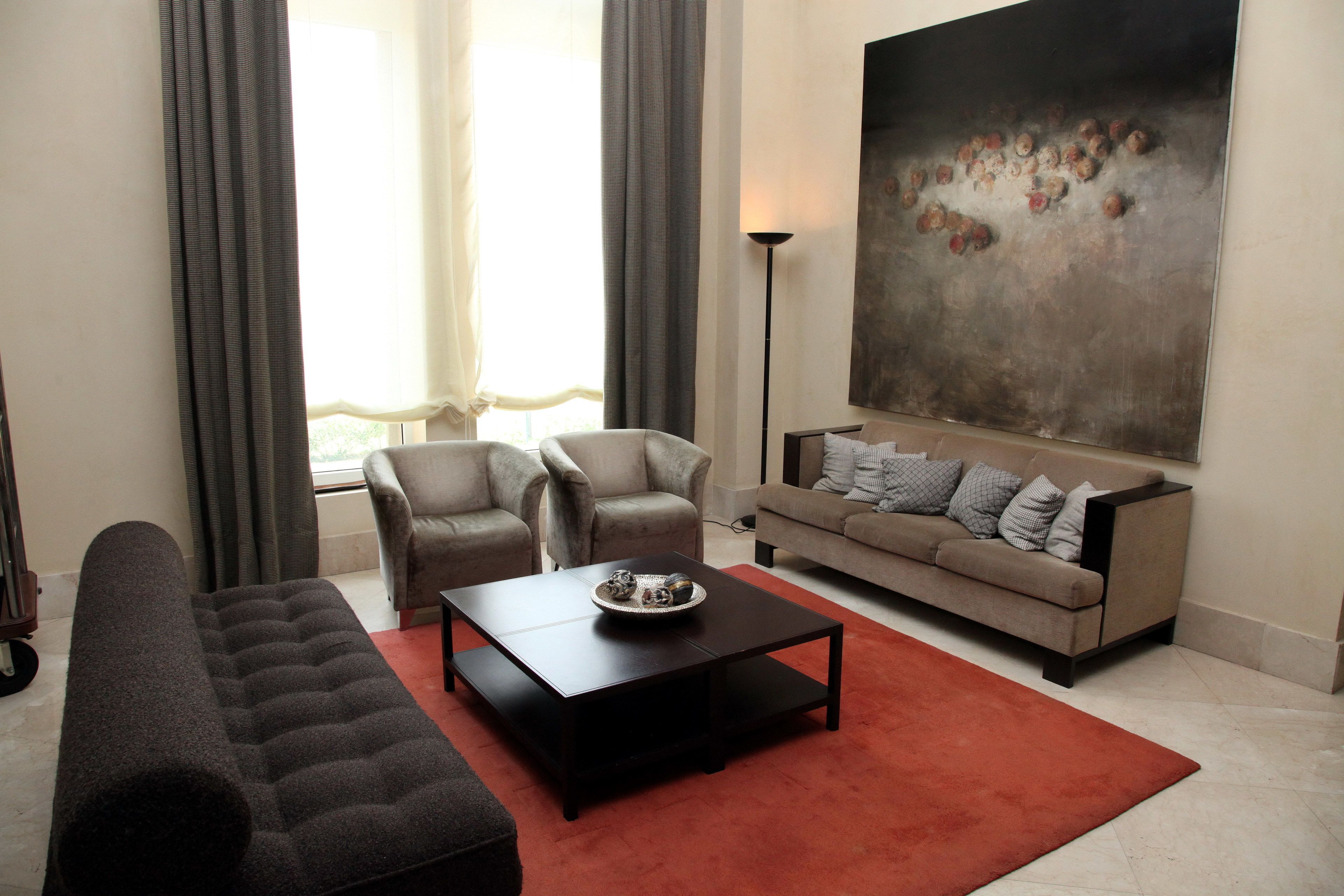 A modern living room with a sofa, armchairs, a coffee table, and a large abstract painting on the wall.
