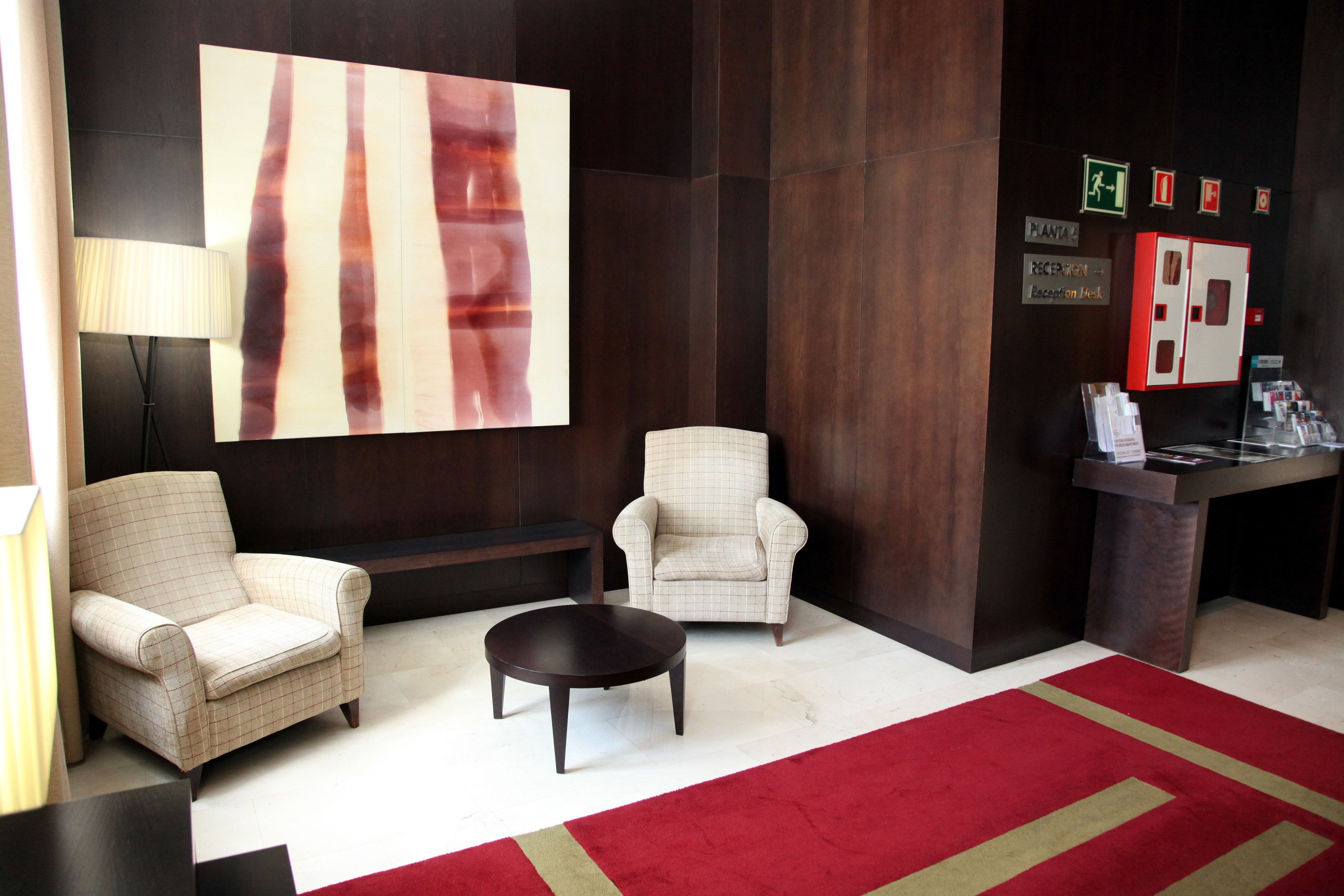 A lobby with two armchairs, a coffee table, a reception desk, and a large abstract painting on the wall.