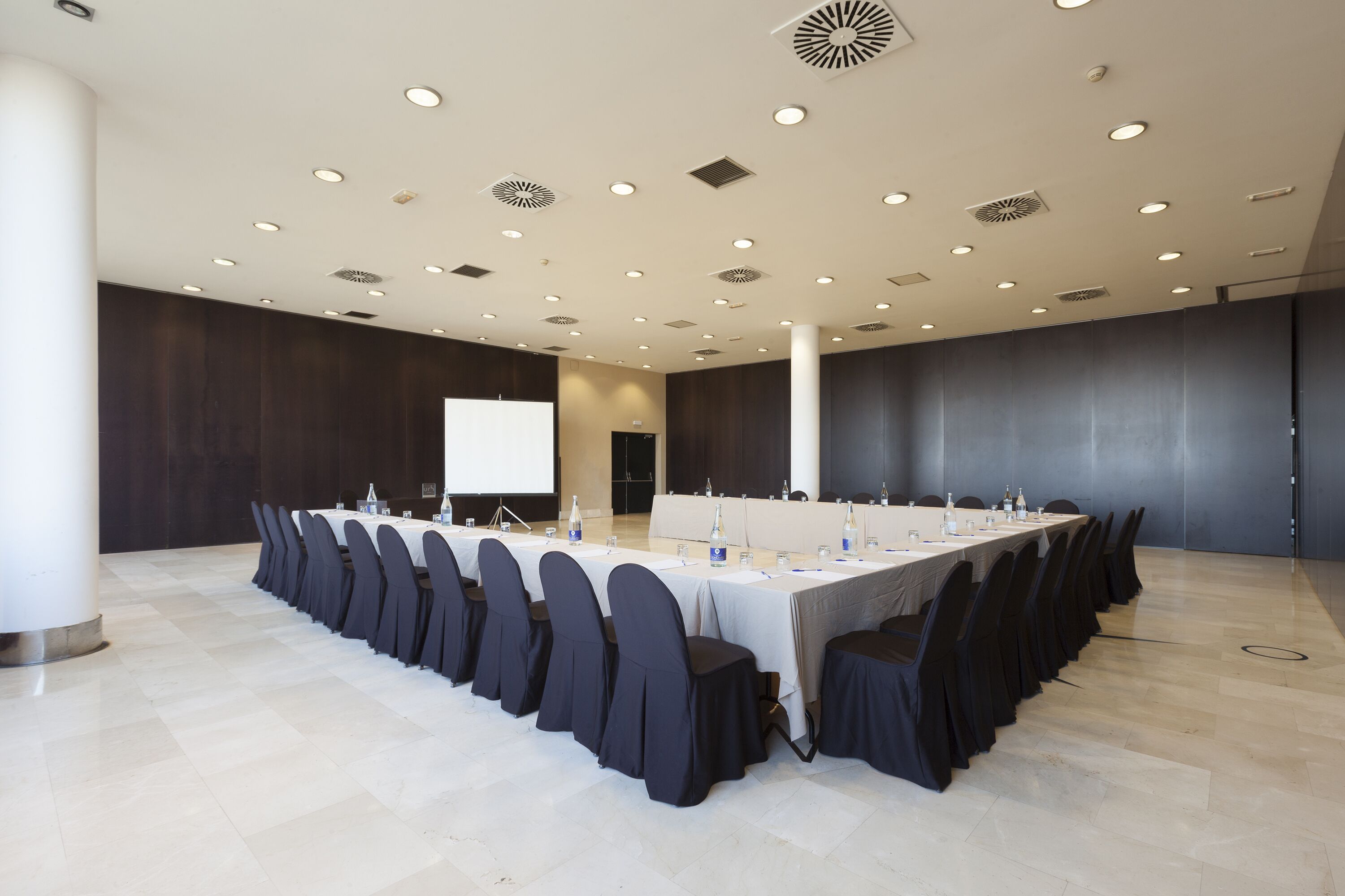 Un salón de conferencias con una mesa larga, sillas y una pantalla para proyector.