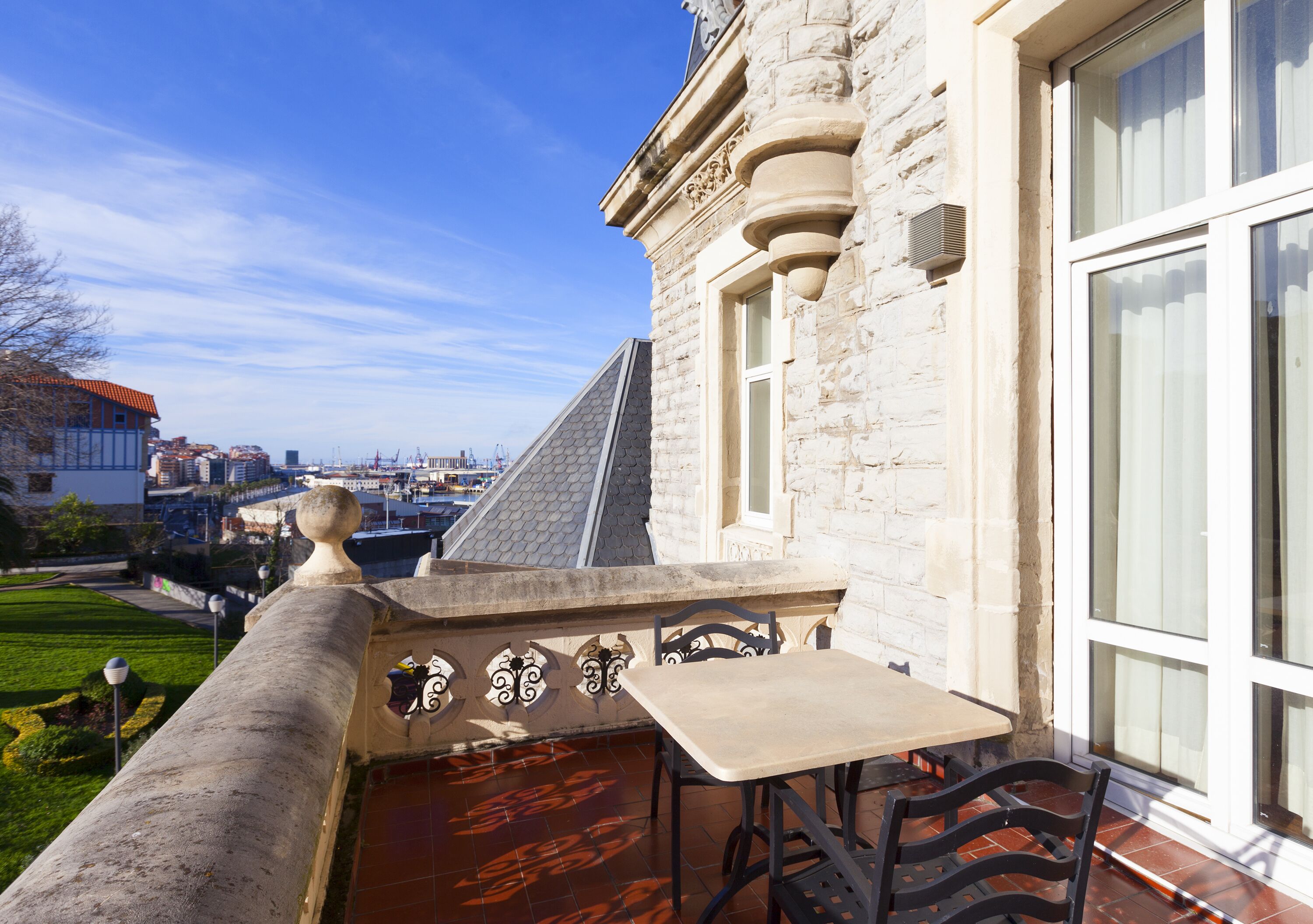 Edifici de pedra amb un balcó que ofereix taula i cadires, amb vista a un paisatge urbà.
