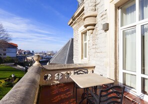 Edificio de piedra con balcón que tiene una mesa y sillas, con vista a un paisaje urbano.