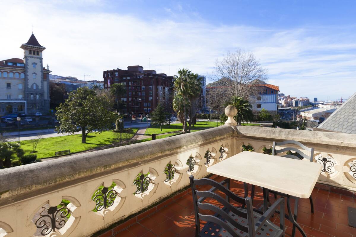 Eine Terrasse mit Tisch und Stühlen, mit Blick auf eine Stadtlandschaft mit Gebäuden und einem Park.