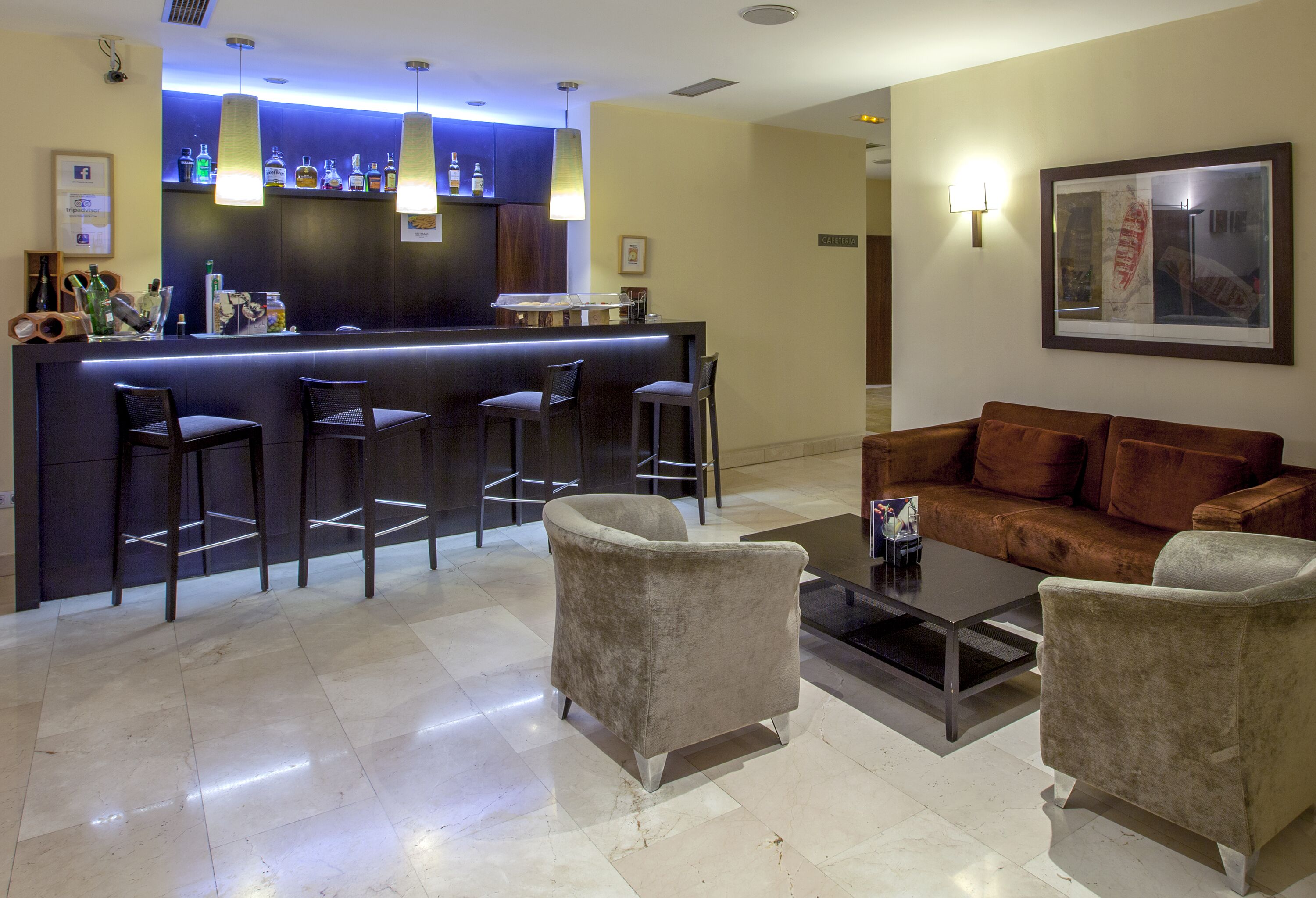 Un área de bar con mostrador y taburetes, un sofá marrón y una mesa de centro en un interior moderno.
