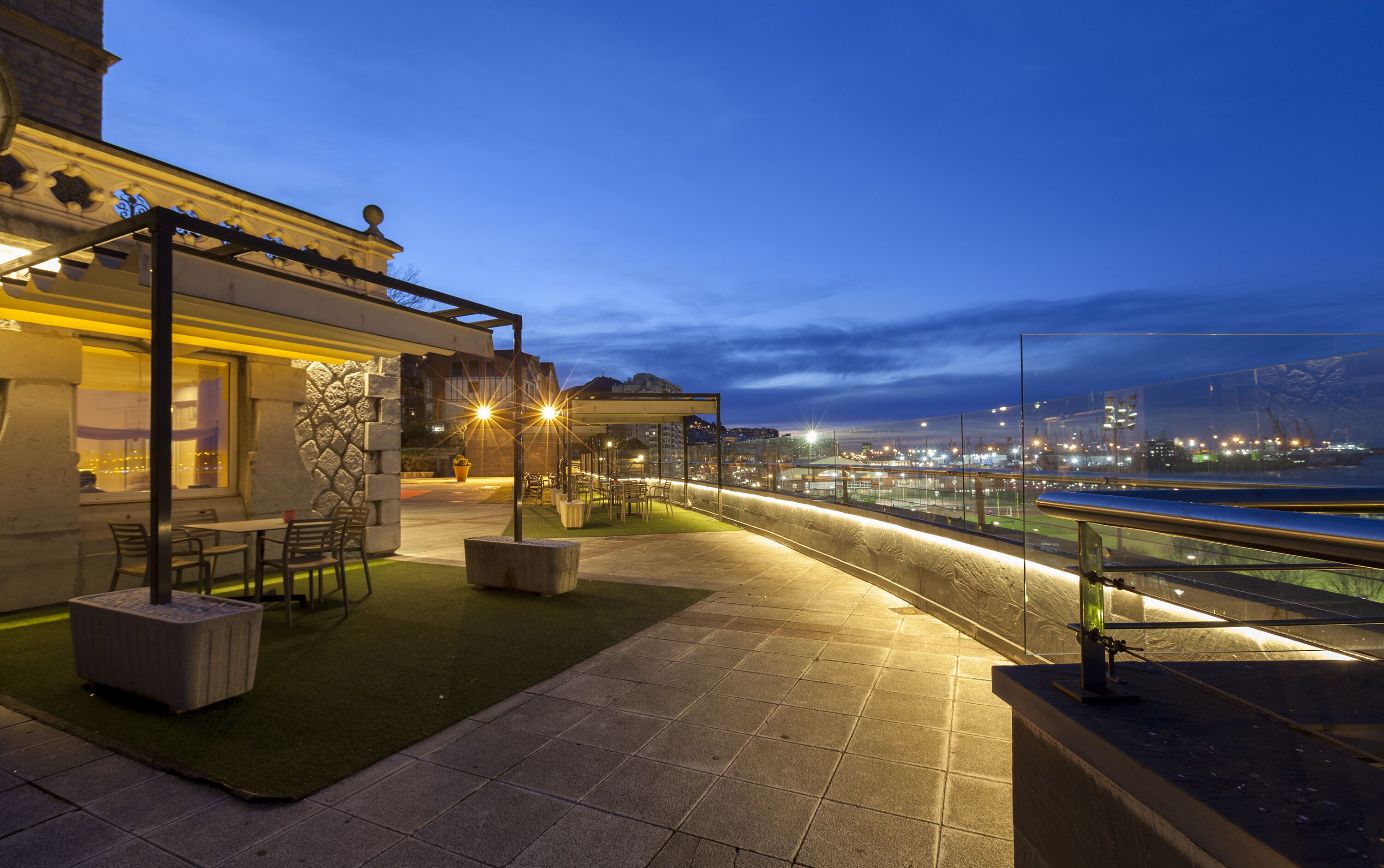 An outdoor terrace with seating, a view of the city skyline, and a river.