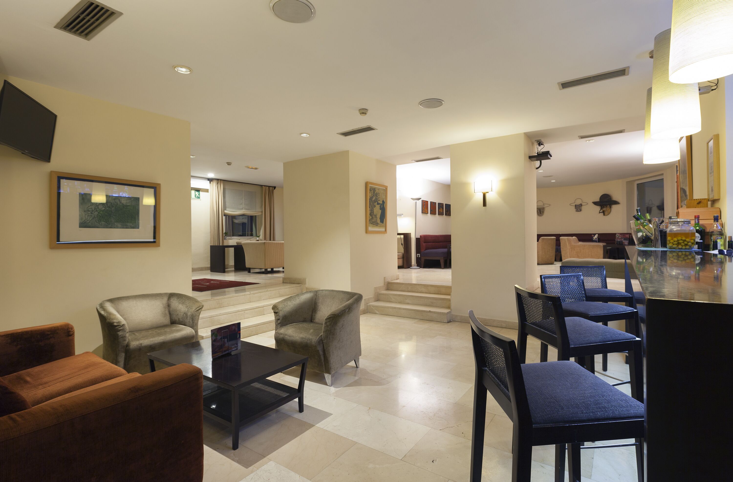 Vestíbulo de hotel con una zona de estar, un bar y una escalera que lleva a un piso superior.
