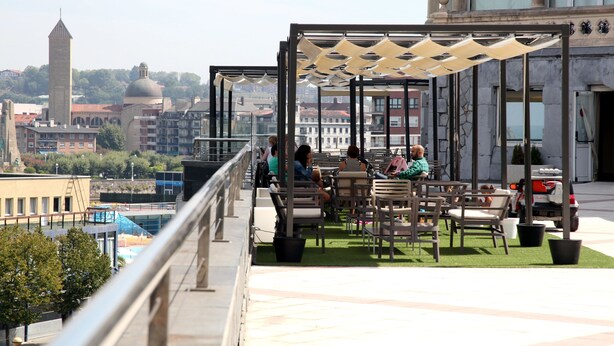 Une terrasse sur le toit, dotée d’un espace extérieur aménagé et offrant une vue sur le paysage urbain, notamment sur une tour et des immeubles.