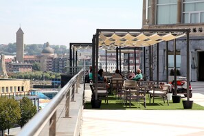 Una terraza en la azotea con mobiliario exterior y vistas a la ciudad, incluyendo una torre y edificios.