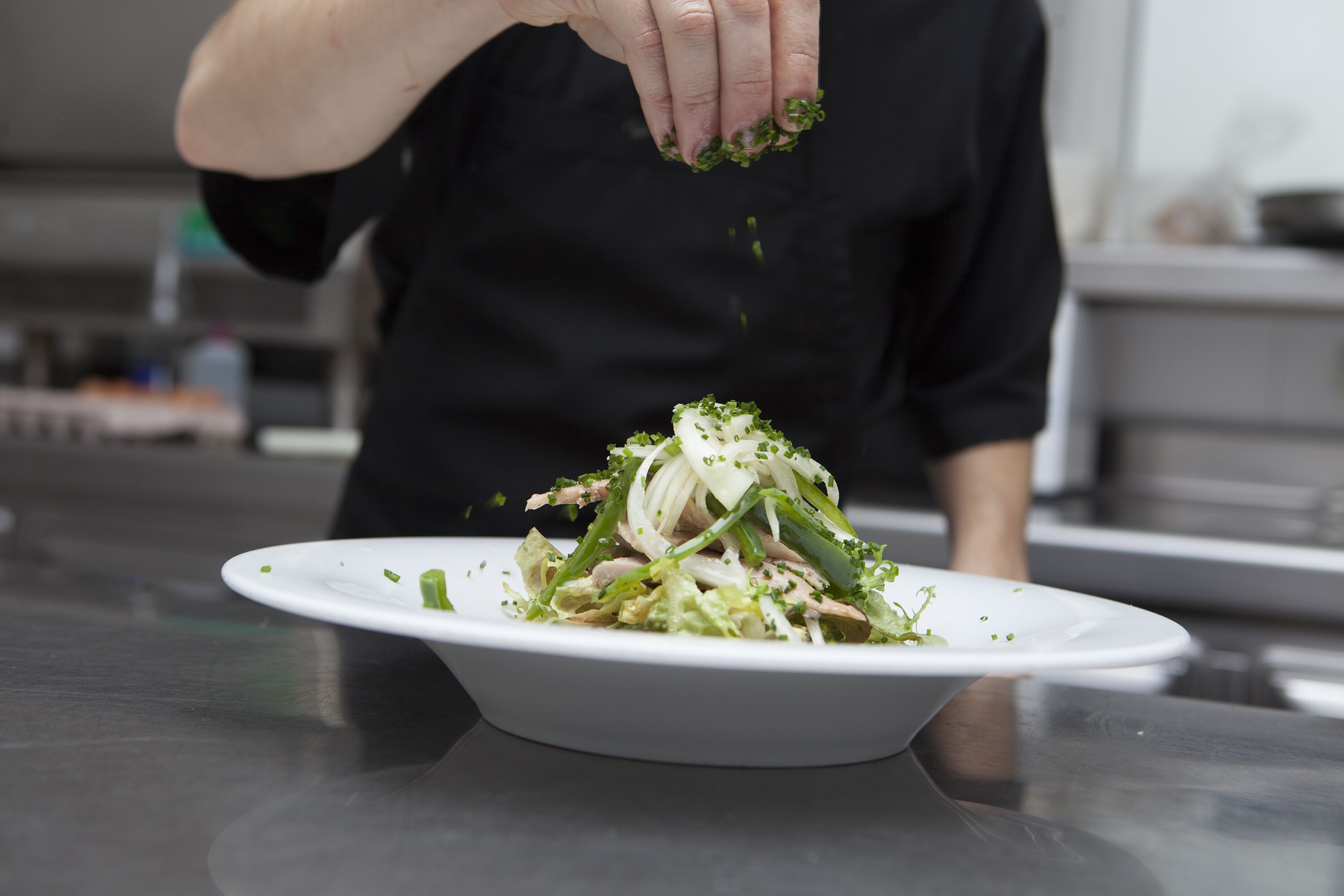 Uno chef spolvera erbe tritate su un piatto bianco.