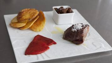 A white plate with food items including a piece of meat, a red item, and a small bowl of chocolate.