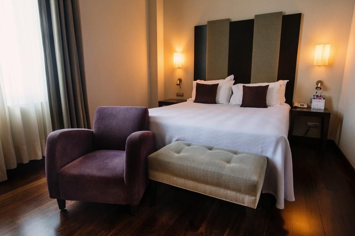 Ein Hotelzimmer mit einem großen Bett, zwei Nachttischen, einem Sessel und einer Bank.