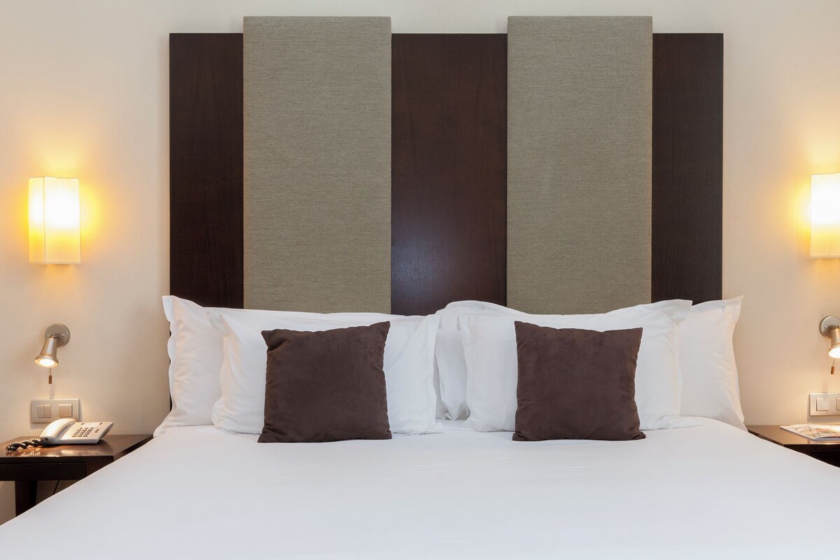 Habitación de hotel con una cama grande, dos mesitas de noche, un teléfono y lámparas fijadas a la pared.