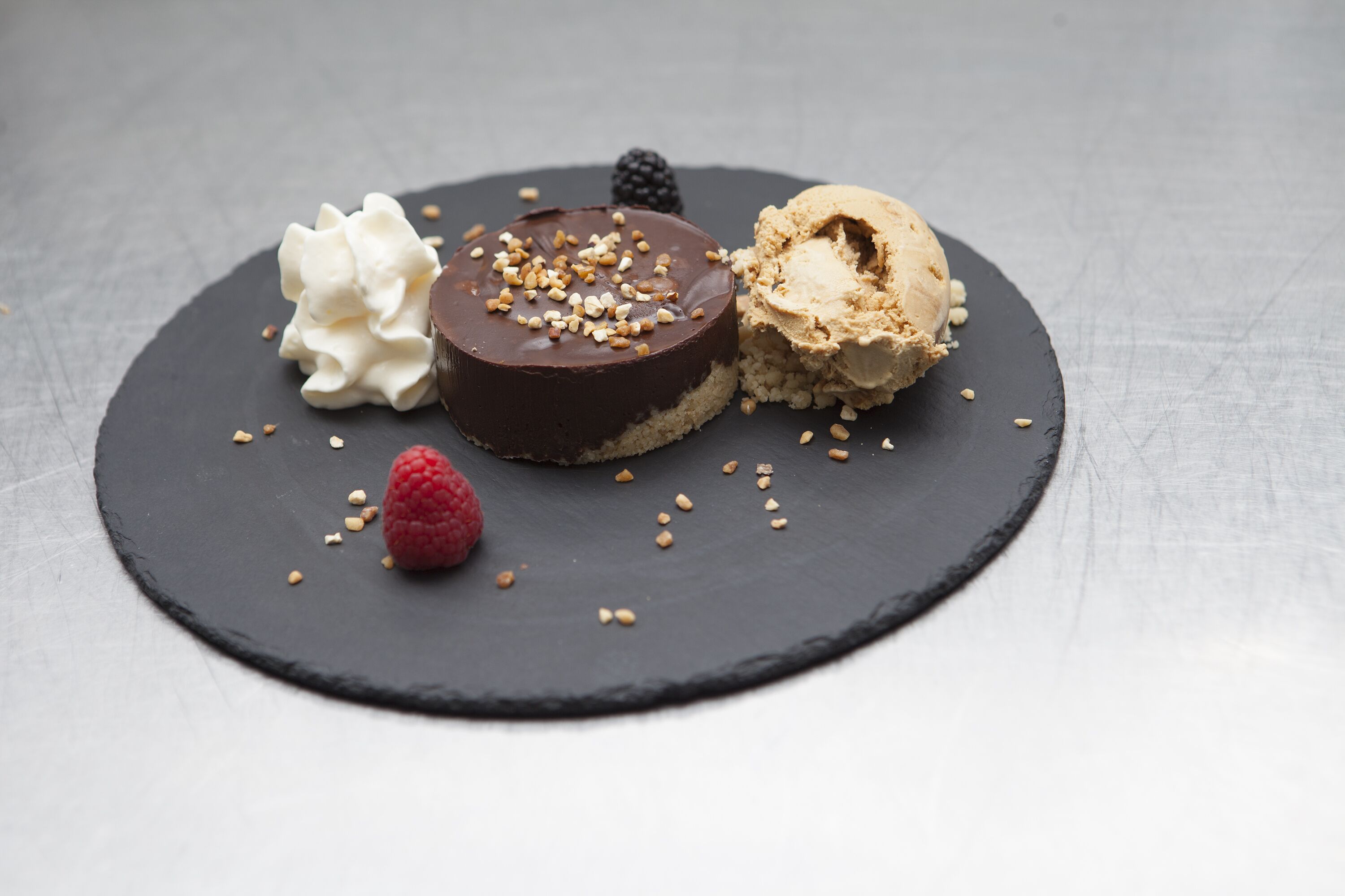 A dessert plate with a chocolate cake, vanilla ice cream, whipped cream, and a raspberry.