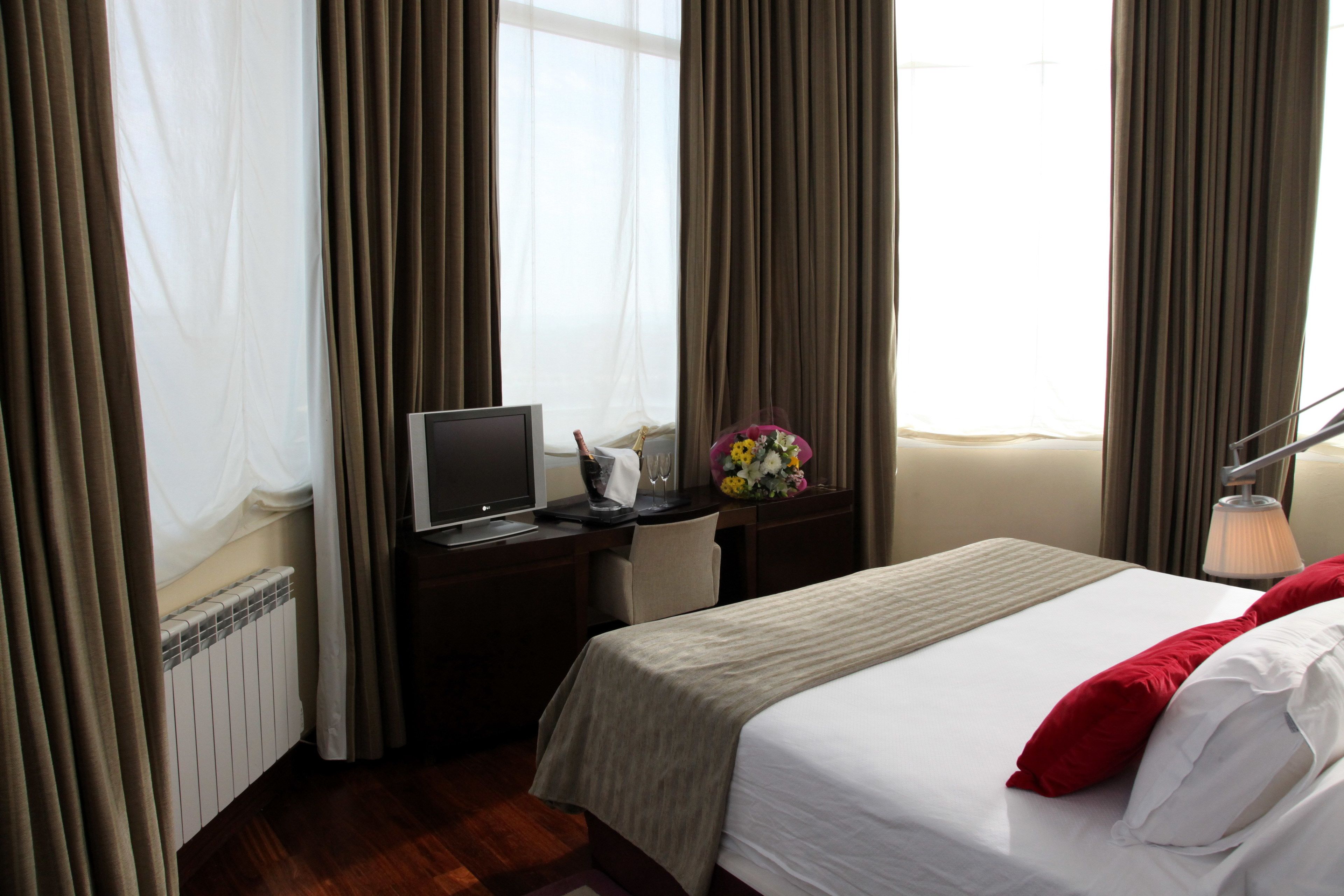 Habitación de hotel con cama, escritorio con computadora, lámpara y ventana con cortinas.