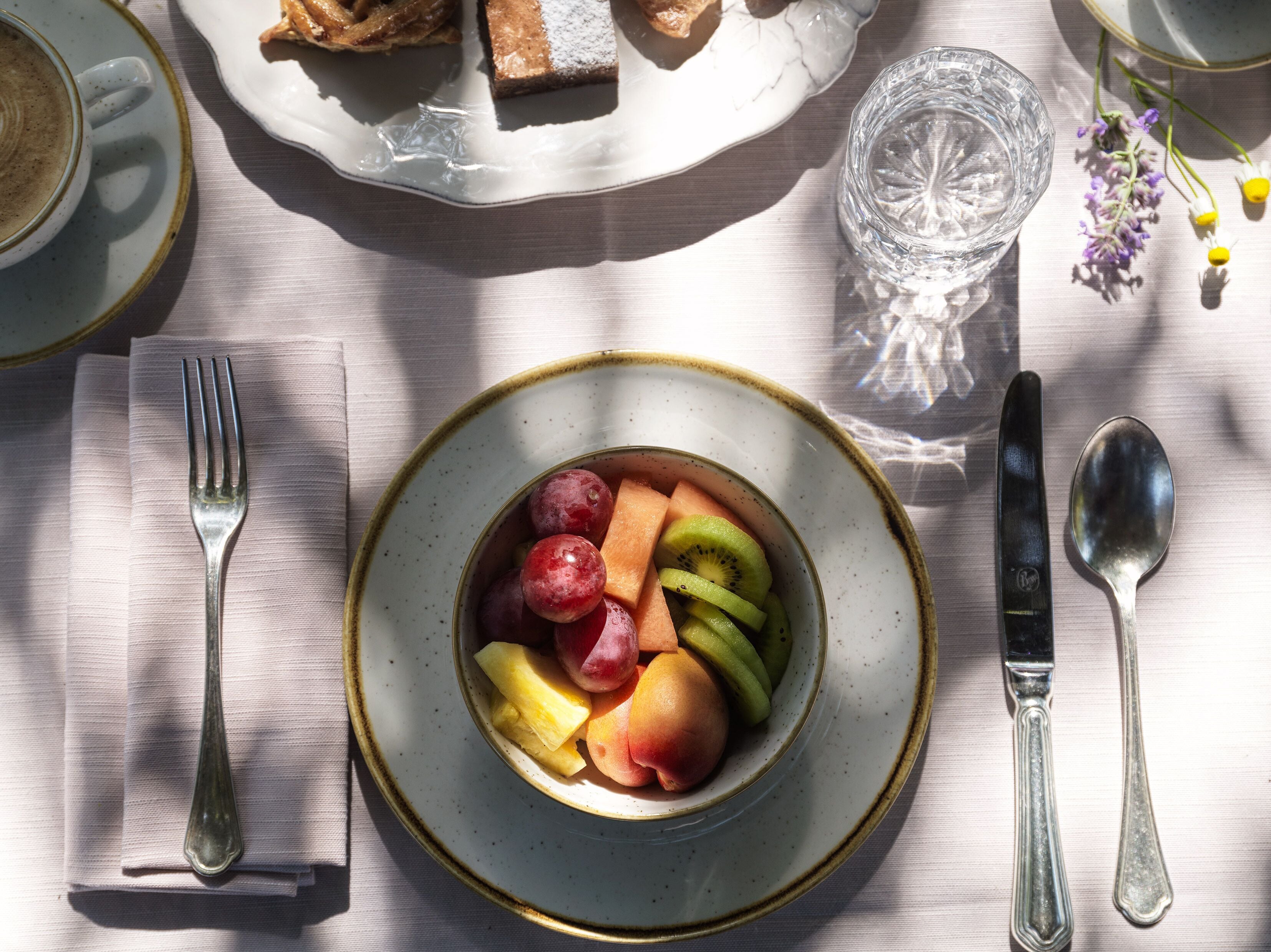 Una mesa dispuesta con una bandeja de fruta, un vaso de agua y cubiertos.