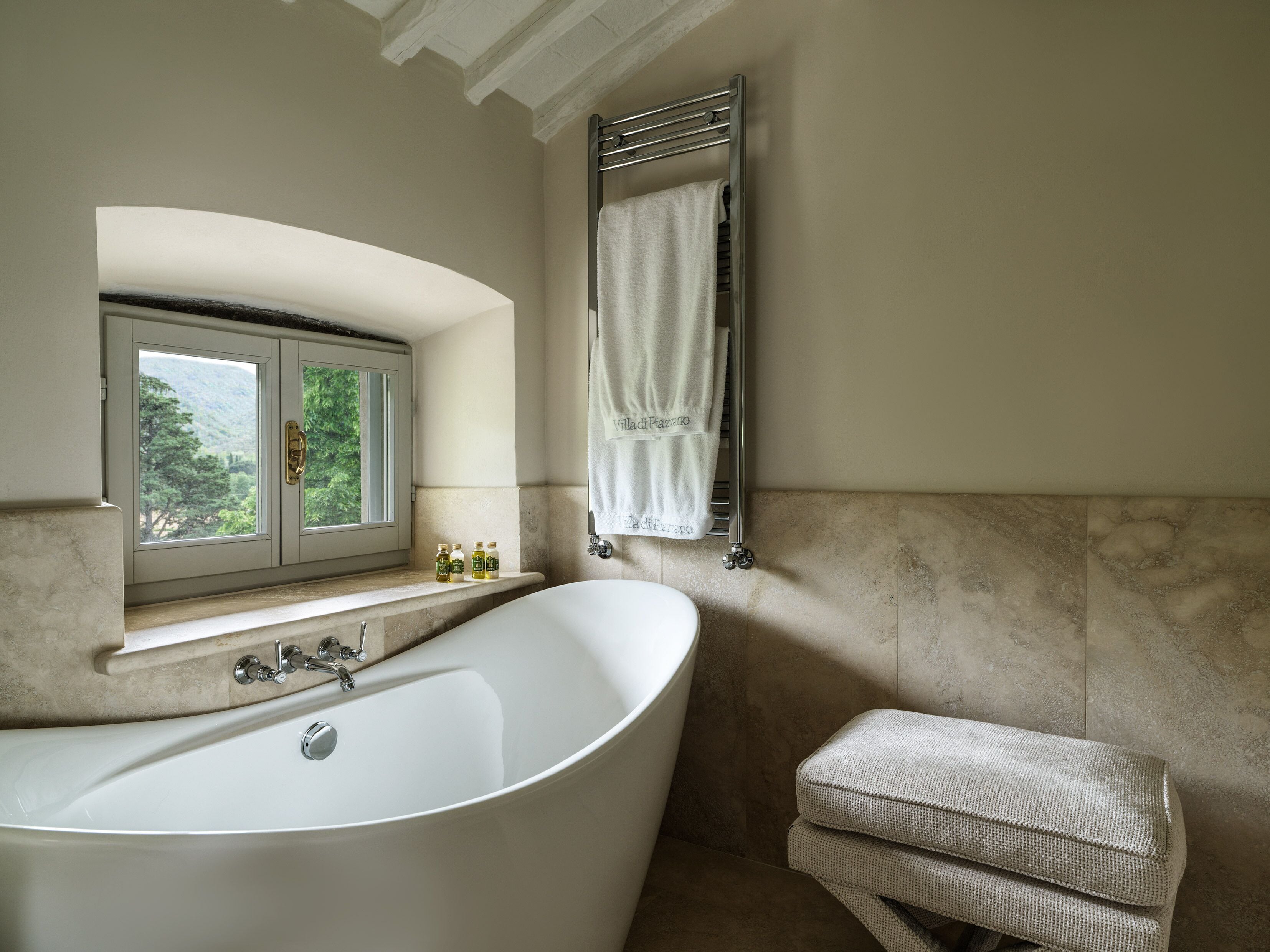 Une salle de bain avec une baignoire sur pieds, une fenêtre donnant sur la verdure et un porte-serviettes avec une serviette.
