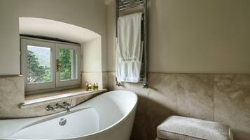 Une salle de bain avec une baignoire sur pieds, une fenêtre donnant sur la verdure et un porte-serviettes avec une serviette.