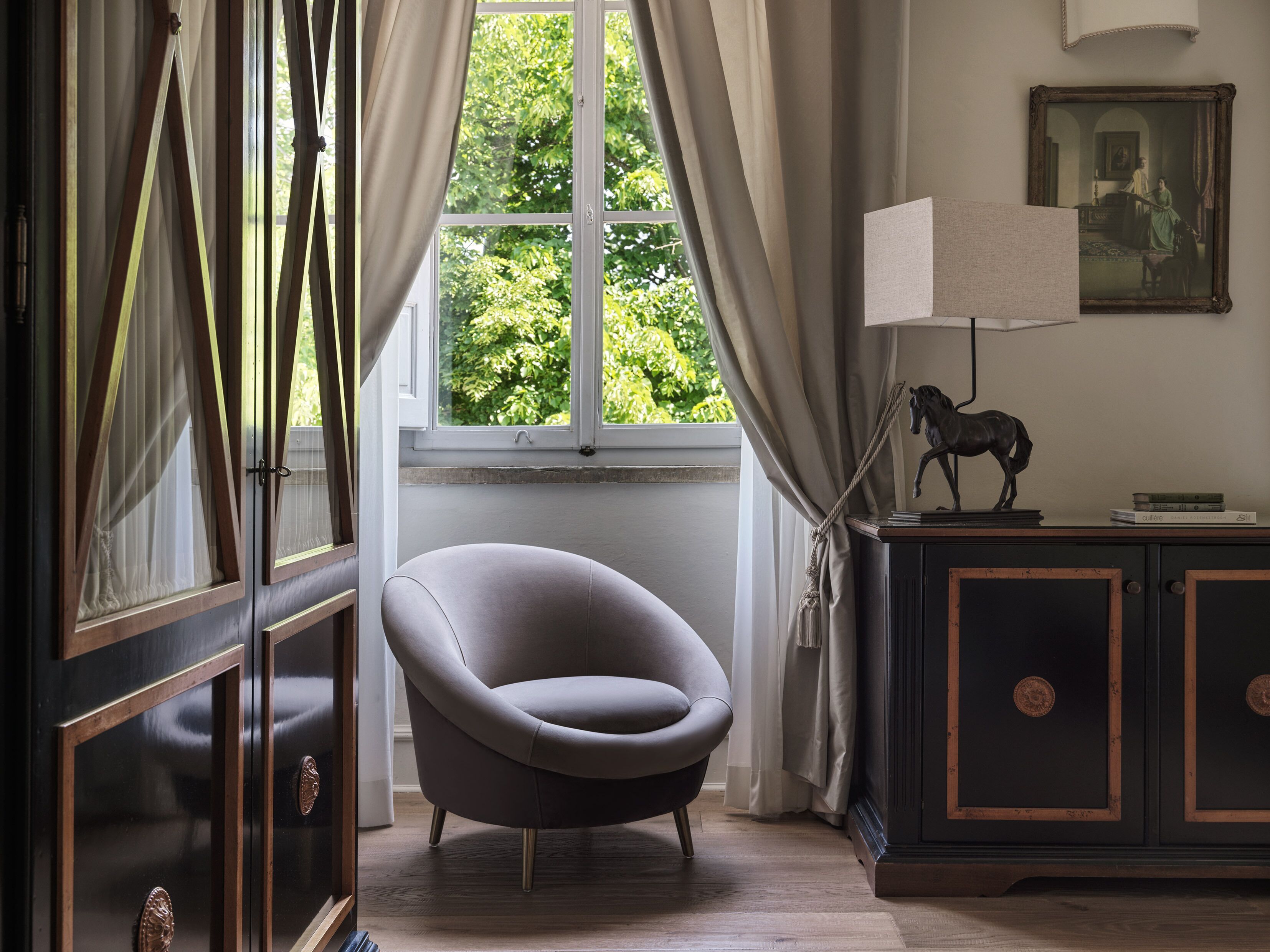 A room with a window, a chair, a lamp, and a cabinet with a horse statue.