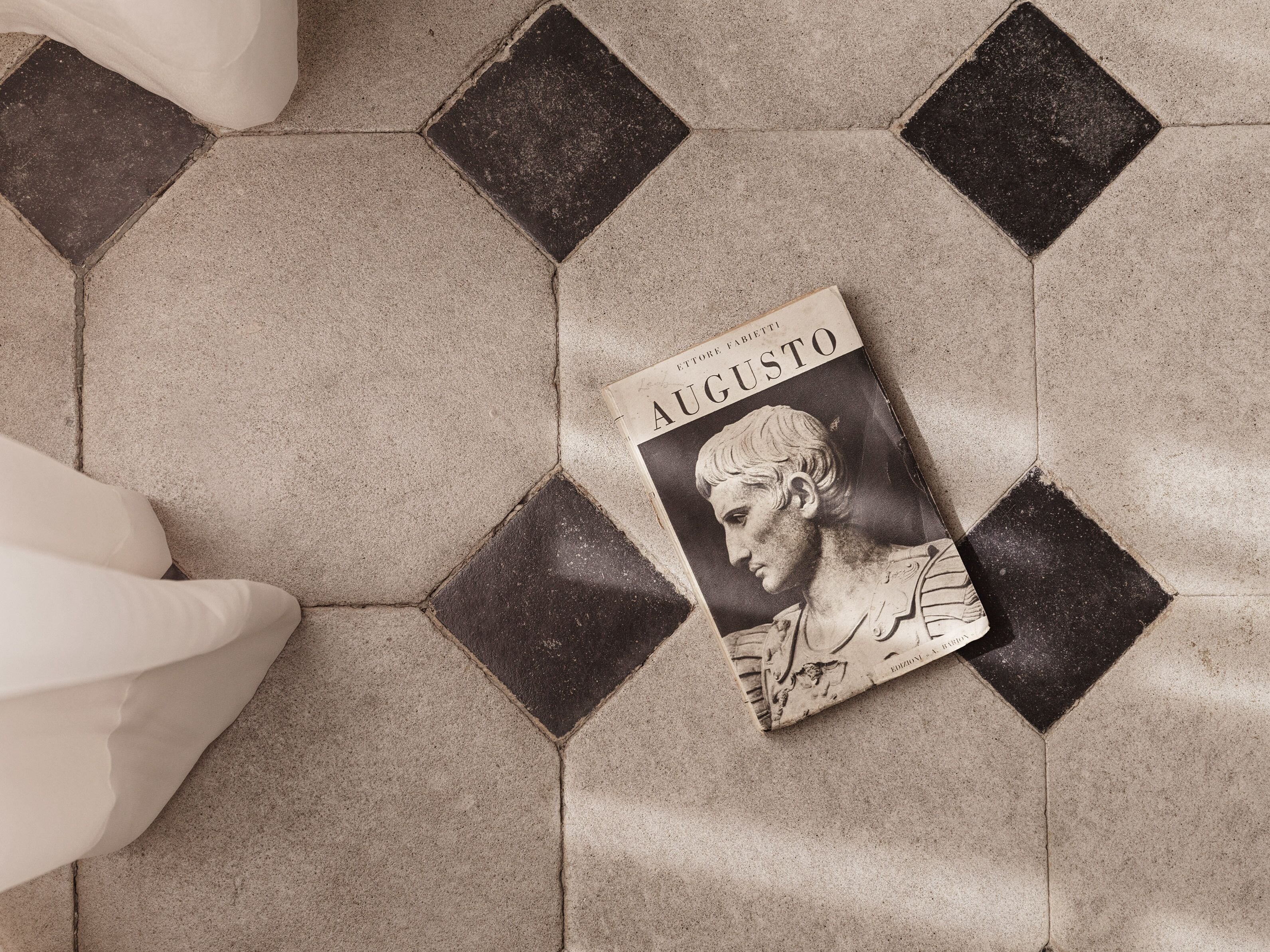 A book titled 'Augusto' placed on a tiled floor with a geometric pattern.