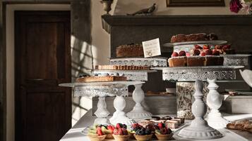 A dessert display with multiple tiers of cakes and fruit tarts on ornate white stands.