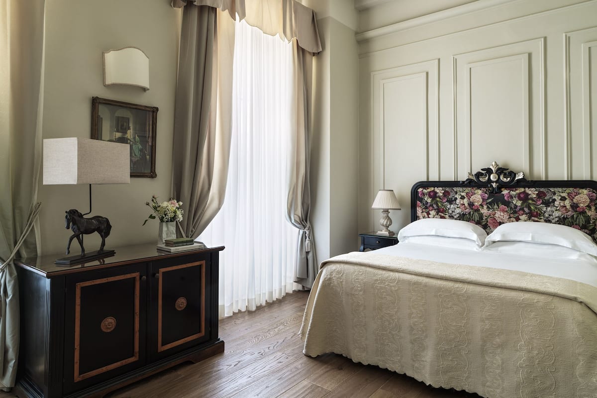 A bedroom with a bed, nightstand, lamp, dresser, and a painting on the wall.