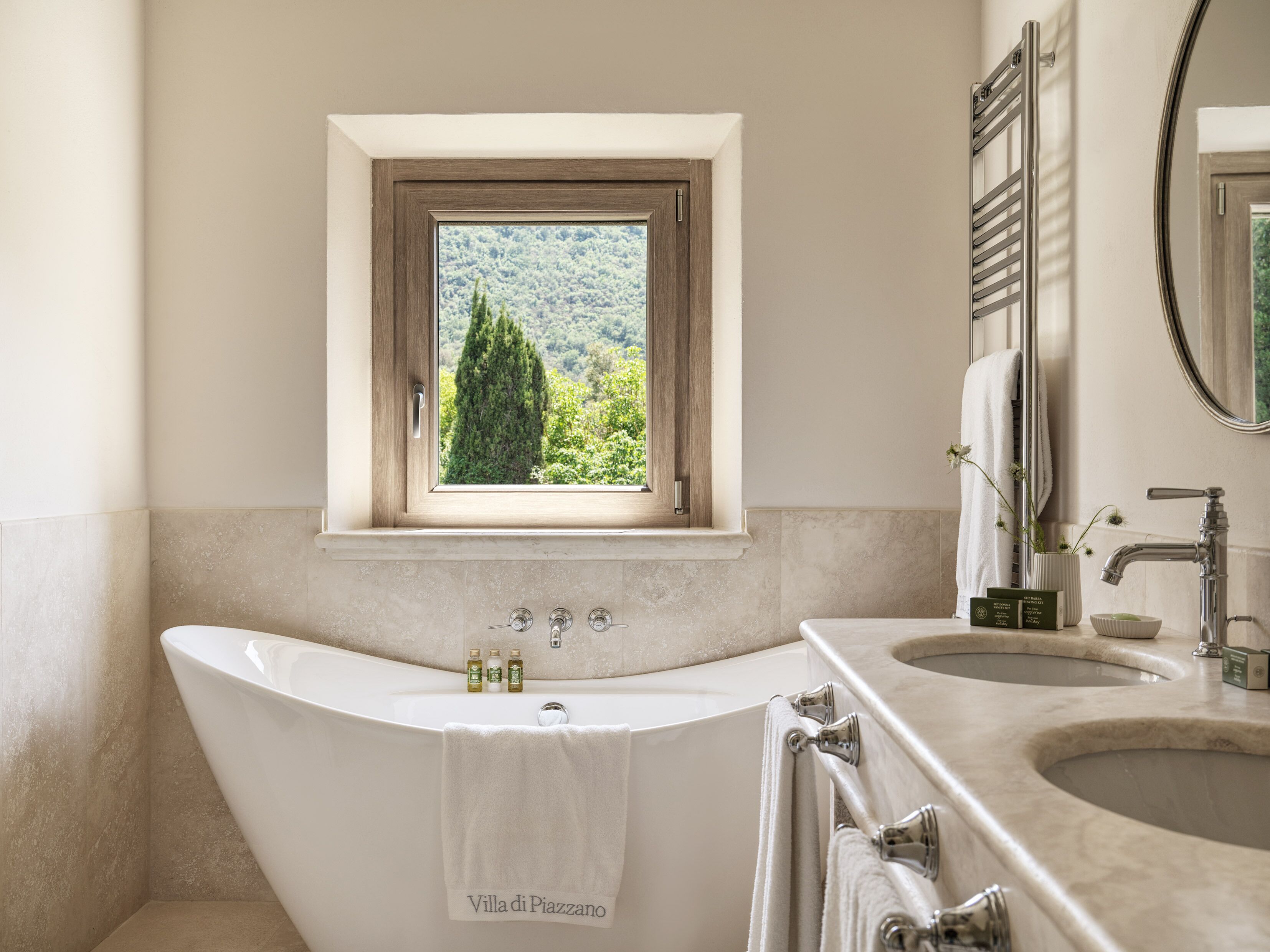 Une salle de bain avec une baignoire sur pieds, une fenêtre donnant sur un espace verdoyant et un meuble-lavabo avec un miroir et un évier.