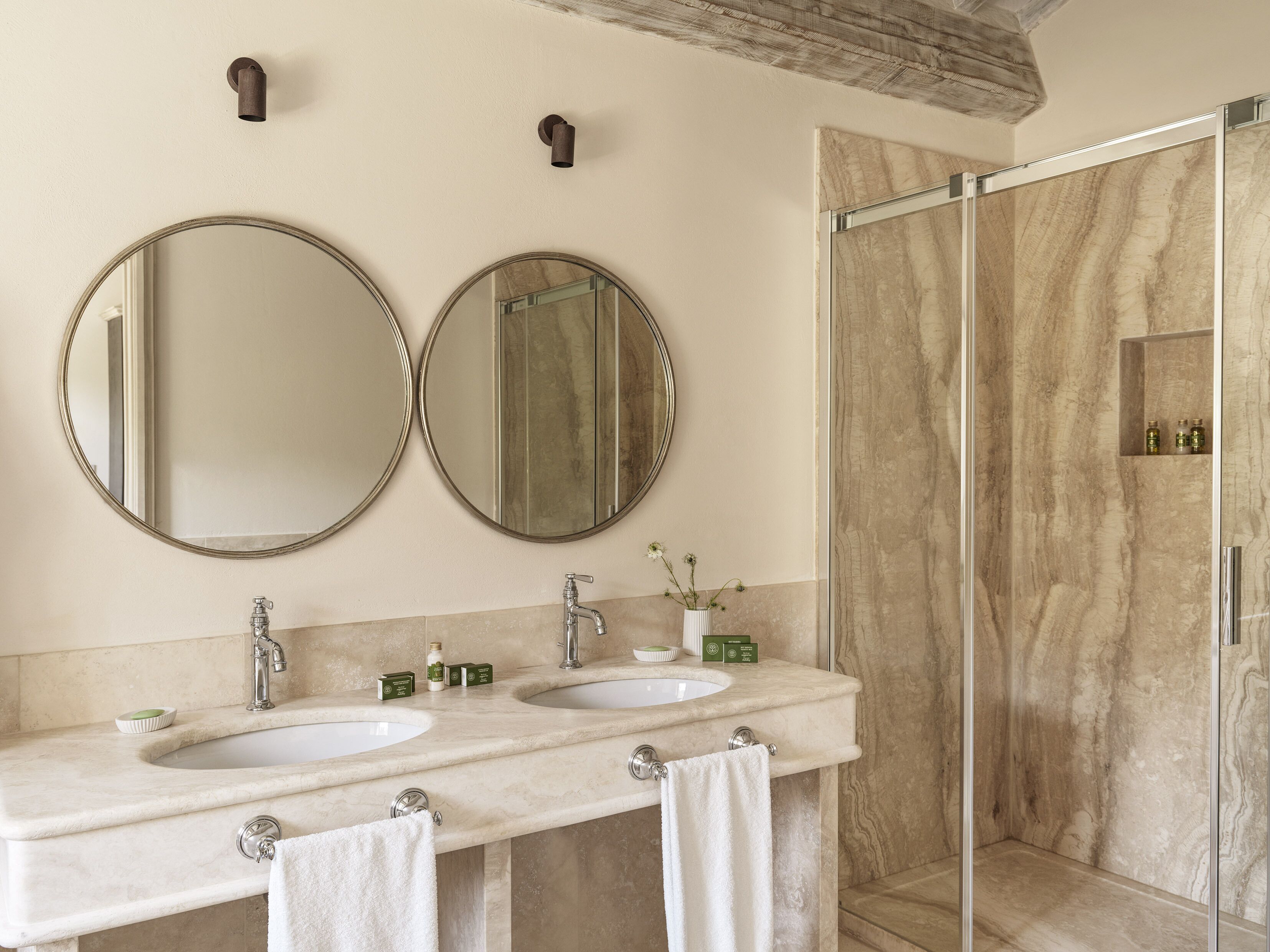 A bathroom with two sinks, two mirrors, a glass shower enclosure, and a marble wall.