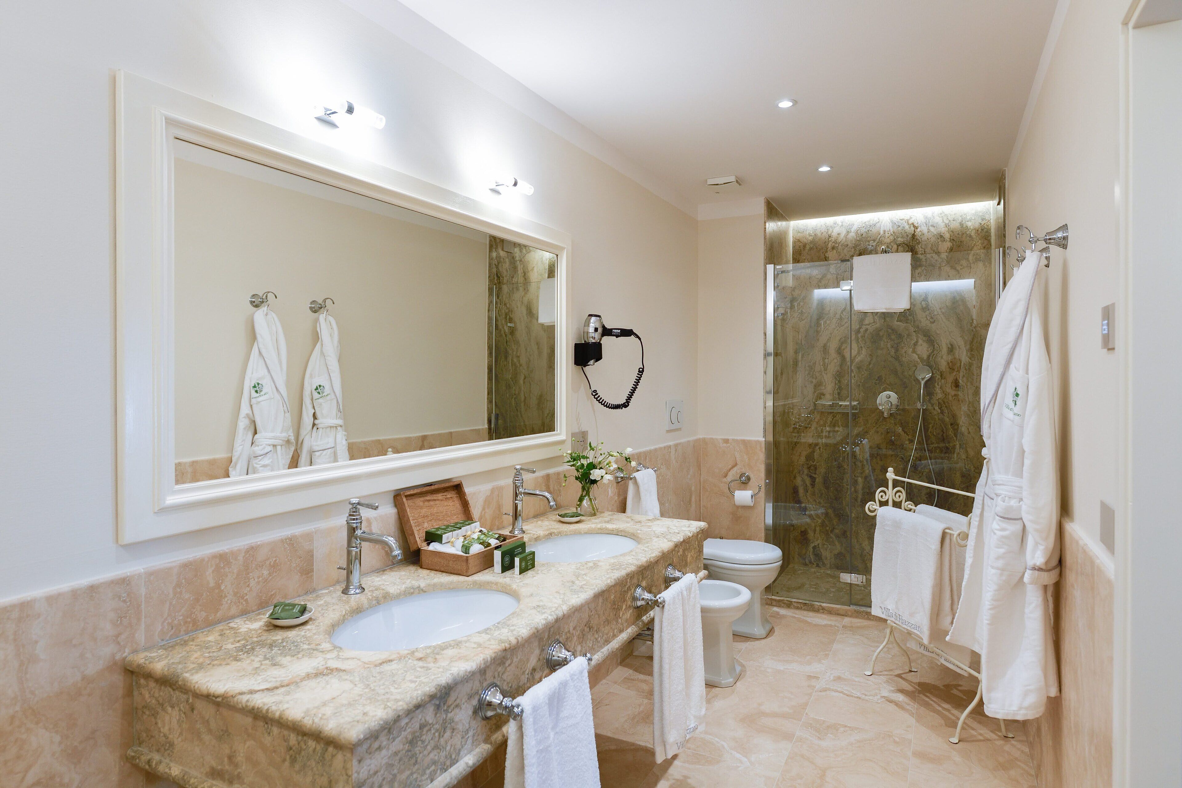 A modern bathroom with two sinks, a large mirror, a hairdryer, and a glass shower enclosure.