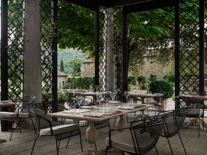Un patio al aire libre con mesas y sillas, rodeado por un cerramiento de celosía y follaje.