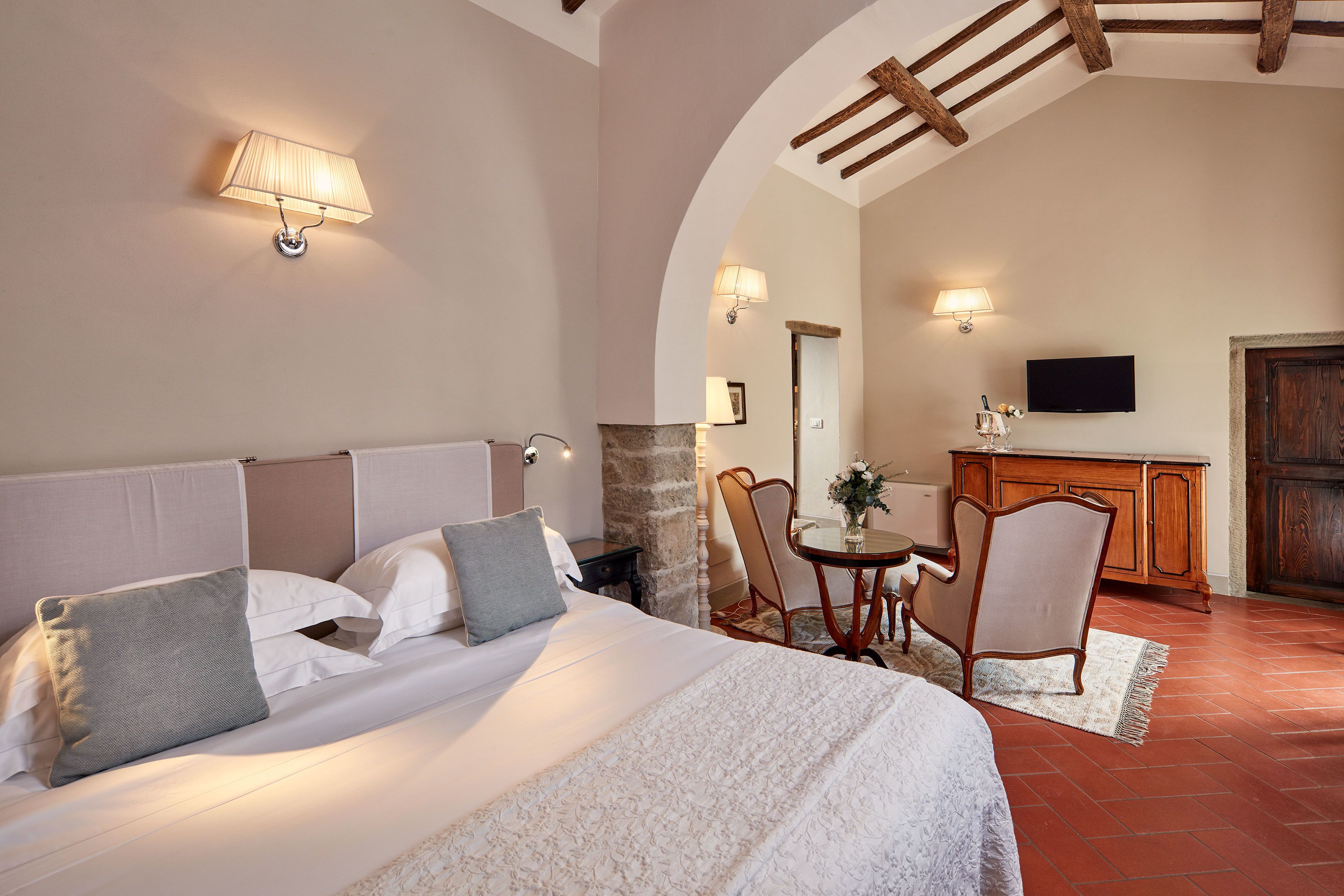 A bedroom with a large bed, two bedside tables, a wooden dresser, a television, and a stone pillar.