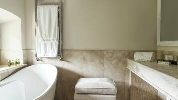 A bathroom with a freestanding bathtub, a towel rack with a towel, a bench, and toiletries on the countertop.