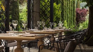 An outdoor dining area with tables set for a meal, surrounded by greenery and trees.