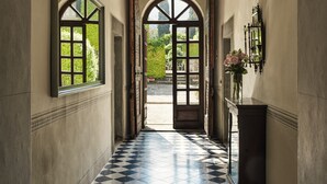 A hallway with a checkered floor, arched windows, and a chandelier.