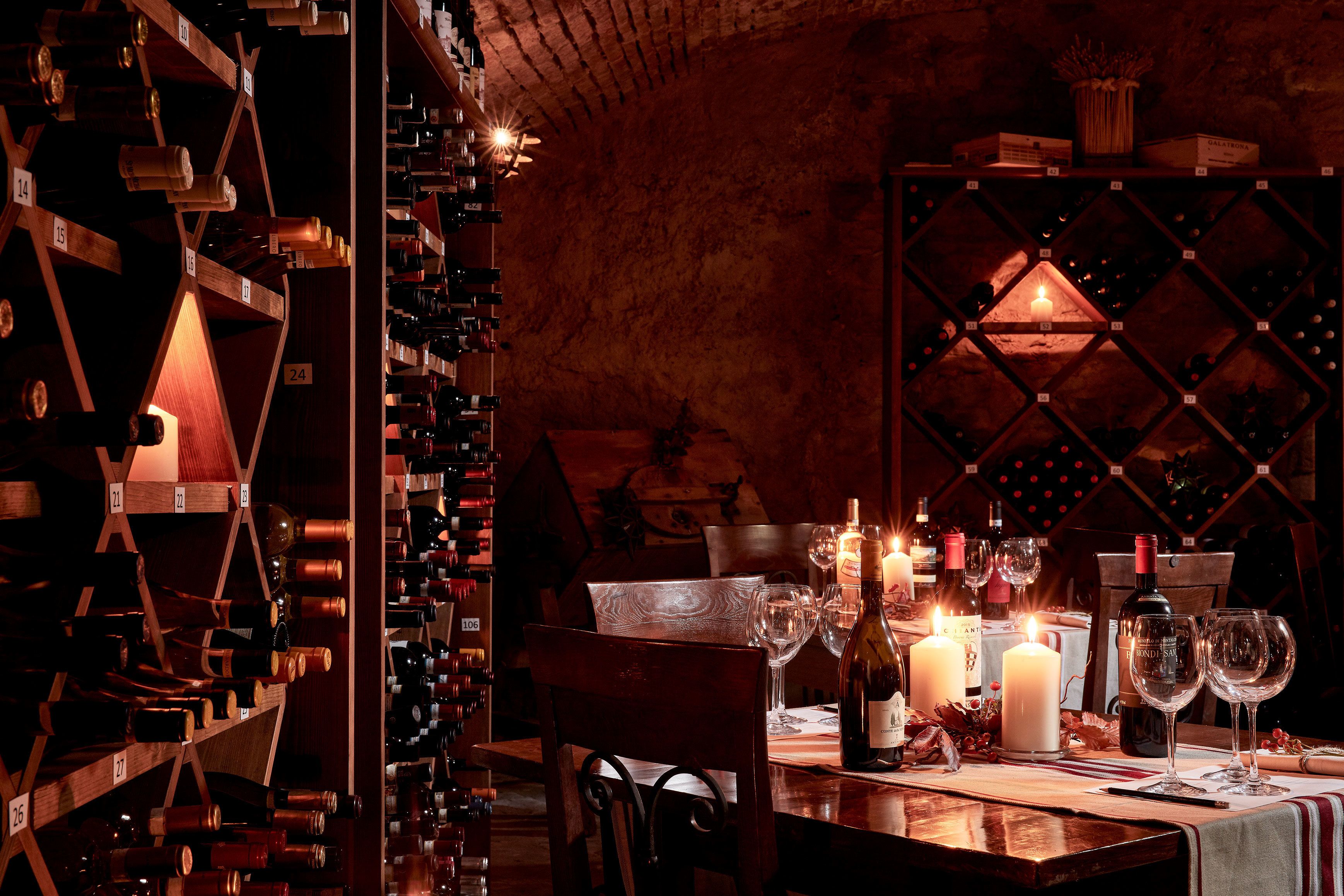 Une cave à vin avec des étagères en bois et une table préparée pour une dégustation de vins, comprenant des bouteilles de vin, des verres et des bougies.