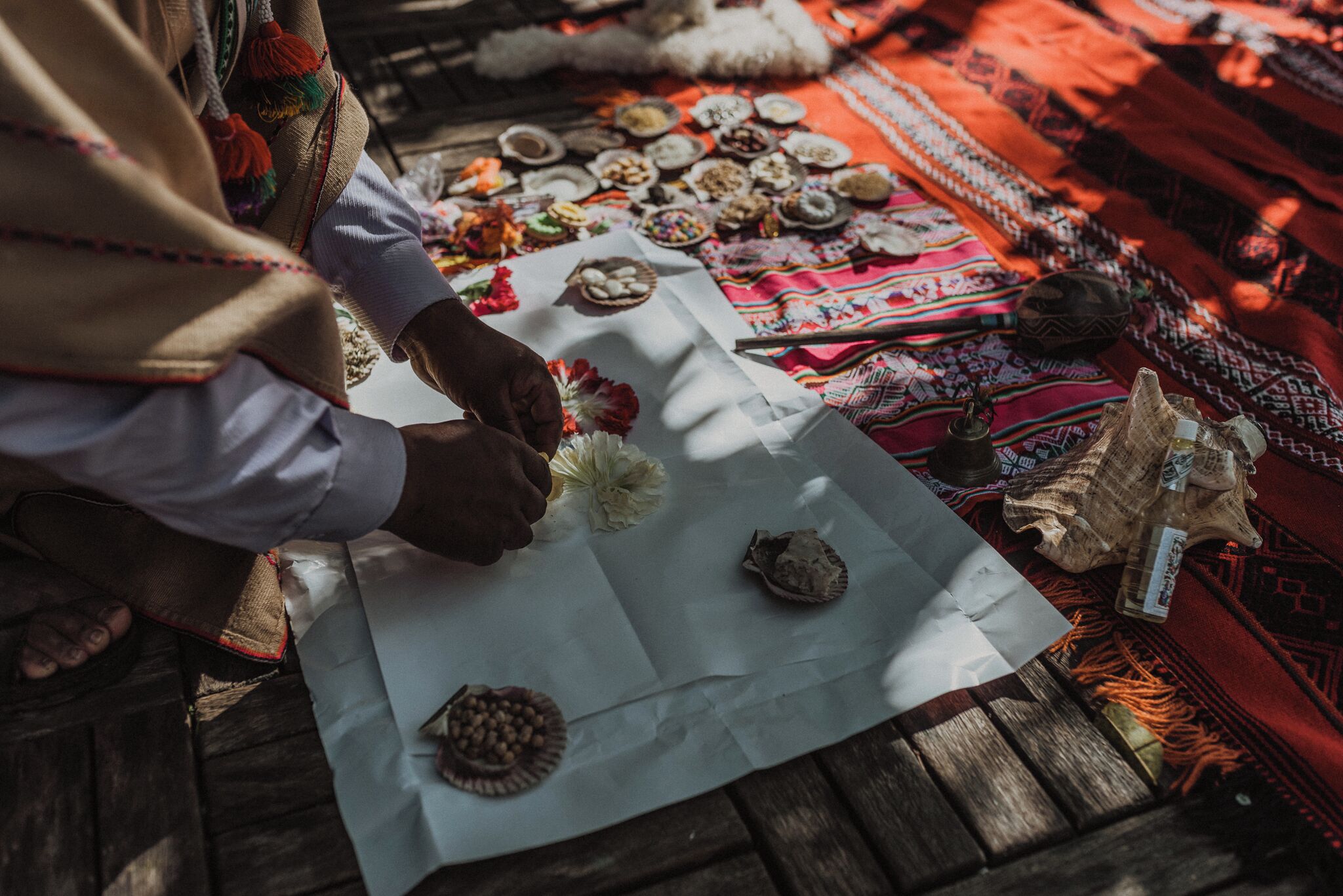 A person arranging items on a table with various objects and a patterned cloth.