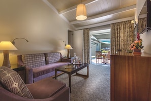 A modern living room with a sofa, armchair, and coffee table, a wooden reception desk, and a view of the outdoor area through a doorway.