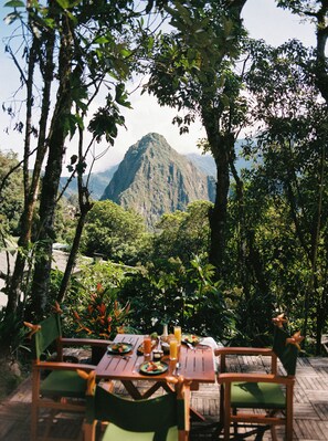 An outdoor dining area with a table set for two, surrounded by lush greenery and overlooking a mountainous landscape. - Sanctuary Lodge, A Belmond Hotel, Machu Picchu (Machu Picchu)