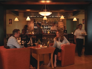 A bar area with a stone wall, multiple hanging lights, and a bartender serving drinks.