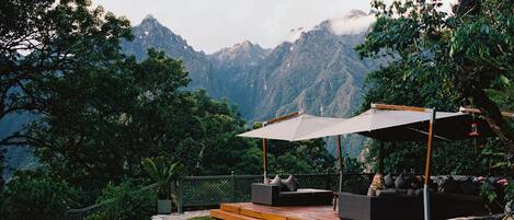 Un espacio exterior con mesas y sillas y vistas a una cadena montañosa.