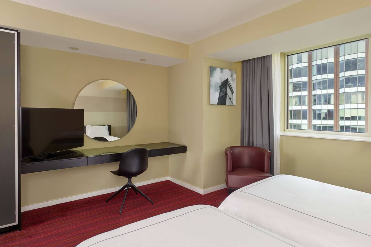 A hotel room with a bed, a desk with a chair, a television, a mirror, a window with curtains, and a painting on the wall.