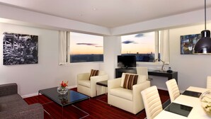 A modern living room with a sofa, armchairs, a coffee table, and a dining area with chairs. There are large windows with a cityscape view. - Park Plaza Leeds (Leeds)
