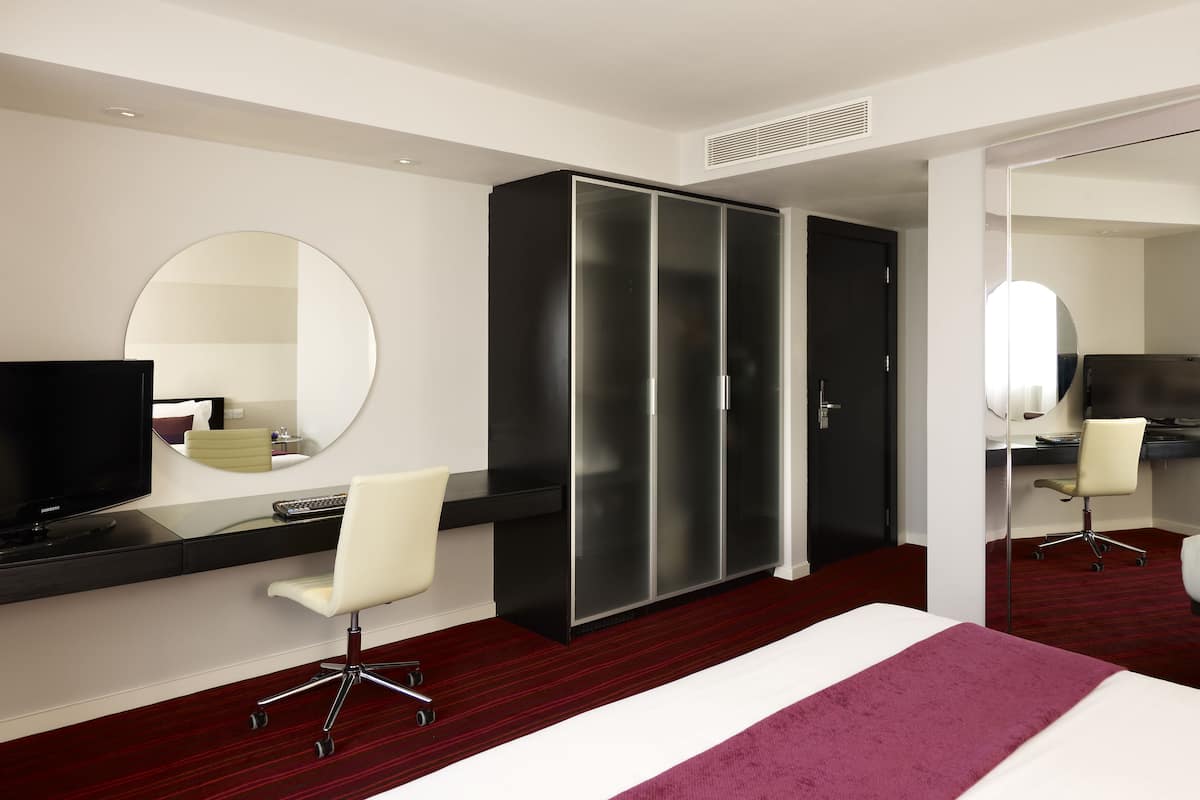 A hotel room with a bed, a desk with a computer, a chair, a wardrobe, and a television.