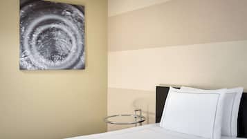 A hotel room with a bed, a round bedside table, a wall-mounted artwork, and a nightstand.